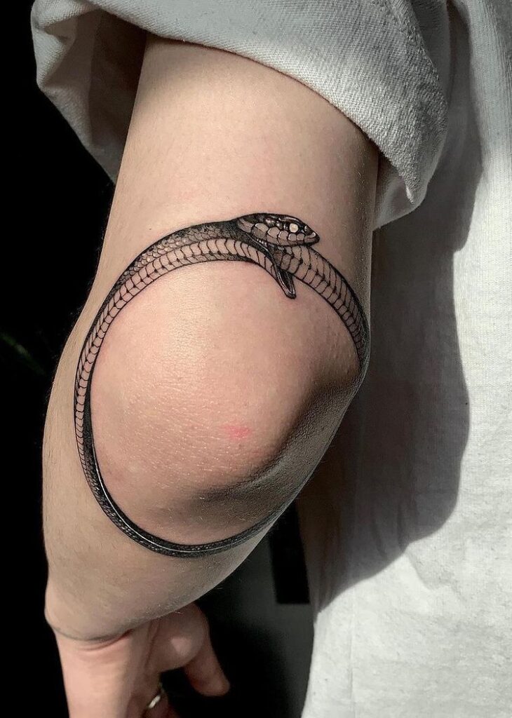Minimalist snake tattoo wrapping around an elbow, showcasing intricate scale detail on bare skin in soft light.