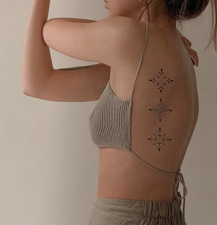 Woman with geometric back tattoo, wearing a beige crop top, showcasing body art and fashion.