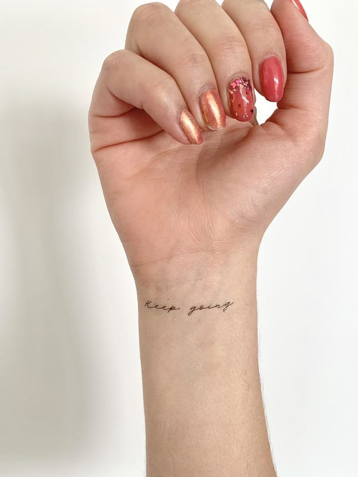 _ 12 Wrist tattoo with keep going text in elegant script and vibrant, glossy pink nails with glitter accent. | Sky Rye Design Wrist tattoo with keep going text in elegant script and vibrant, glossy pink nails with glitter accent.