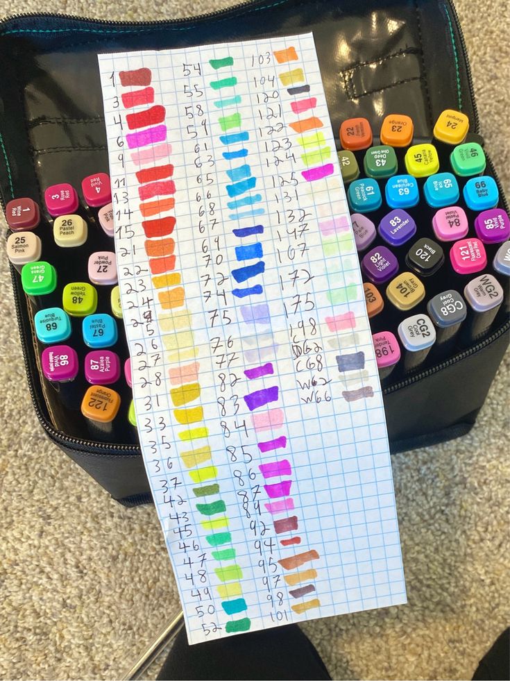 Color-coded marker swatch chart on graph paper beside a case of colorful markers for organization and reference.