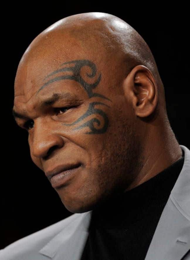 126cc6880da5e73132ab34d0f53c835e Man with face tattoo in a thoughtful pose, wearing a suit jacket. Dark background enhances focus on facial expression and tattoo details. | Sky Rye Design Man with face tattoo in a thoughtful pose, wearing a suit jacket. Dark background enhances focus on facial expression and tattoo details.