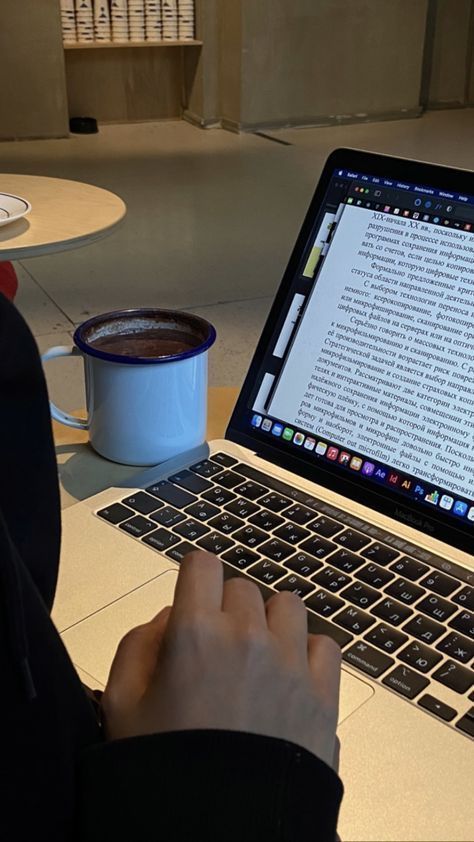 142202d8751c4cf9564cffb939f4f62d Person working on a laptop with text document, coffee mug on the table, cozy workspace setting with shelves in background. | Sky Rye Design Person working on a laptop with text document, coffee mug on the table, cozy workspace setting with shelves in background.