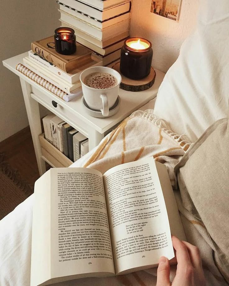 _ 15 Cozy reading nook with an open book, cappuccino, and candlelit ambiance on a bed beside a stack of books on a white nightstand. | Sky Rye Design Cozy reading nook with an open book, cappuccino, and candlelit ambiance on a bed beside a stack of books on a white nightstand.
