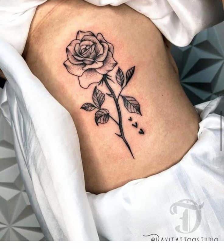 Elegant black and white rose tattoo on ribcage, showcasing intricate shading and delicate leaf details for a classic floral design.