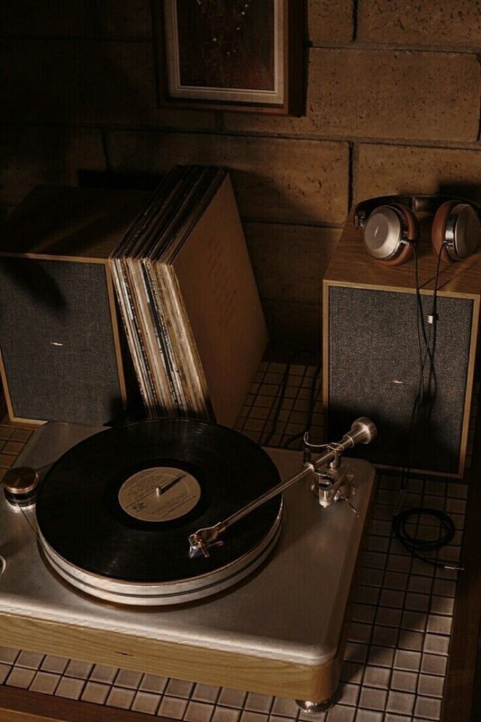Vintage vinyl record player with headphones on a wooden speaker, surrounded by records, creating a nostalgic music atmosphere.
