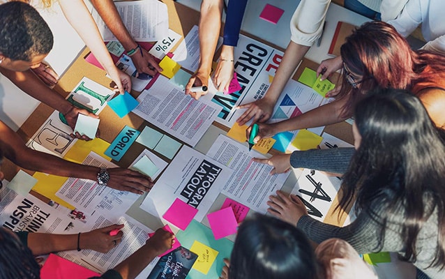 Diverse team collaborating on a creative project with colorful papers and documents spread out on a table, showcasing teamwork and innovation.