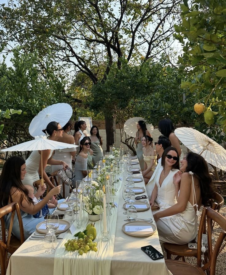 Screenshot Outdoor garden party with people enjoying a long, elegantly set table, adorned with white umbrellas and floral arrangements. | Sky Rye Design Outdoor garden party with people enjoying a long, elegantly set table, adorned with white umbrellas and floral arrangements.