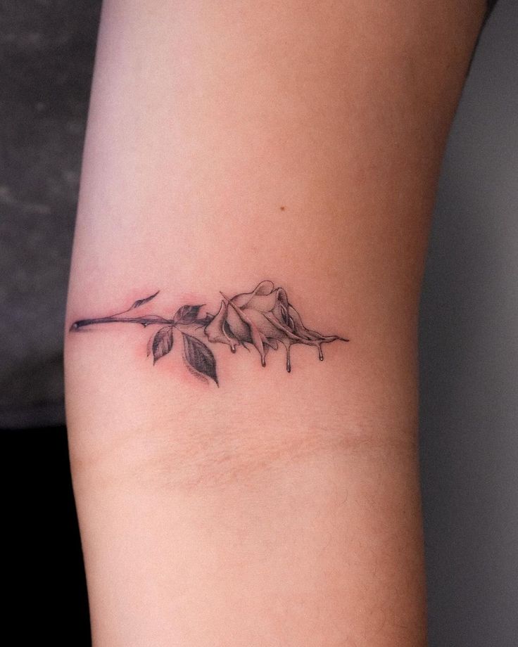 Minimalist rose tattoo with fine lines and delicate shading on forearm, showcasing a unique artistic design.