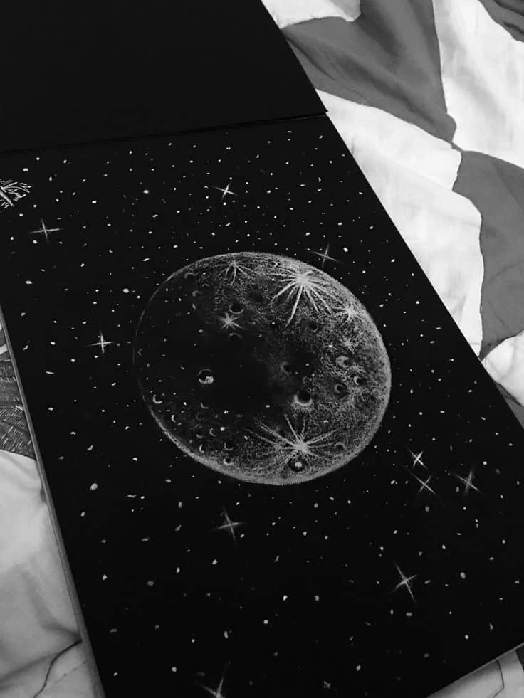 Sketch of a moon surrounded by stars on black paper, showcasing intricate lunar details and a cosmic theme.