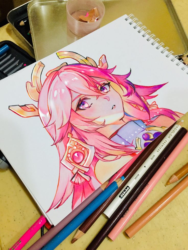 Anime character drawing with pink hair on sketchbook alongside colored pencils.