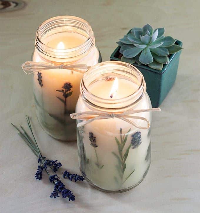 Lit lavender candles in jars with succulents on wooden table, creating a cozy and inviting atmosphere.