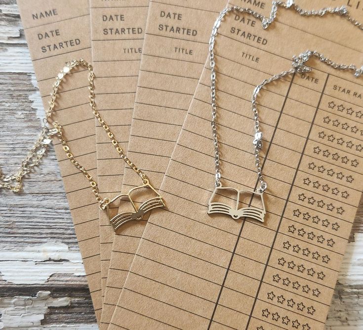 _ 17 Gold and silver open book necklaces on vintage library checkout cards, perfect for book lovers and readers. | Sky Rye Design Gold and silver open book necklaces on vintage library checkout cards, perfect for book lovers and readers.