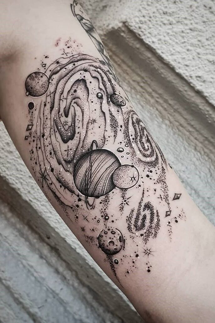 Cosmic tattoo design with planets and galaxies on arm, featuring detailed black ink line art.
