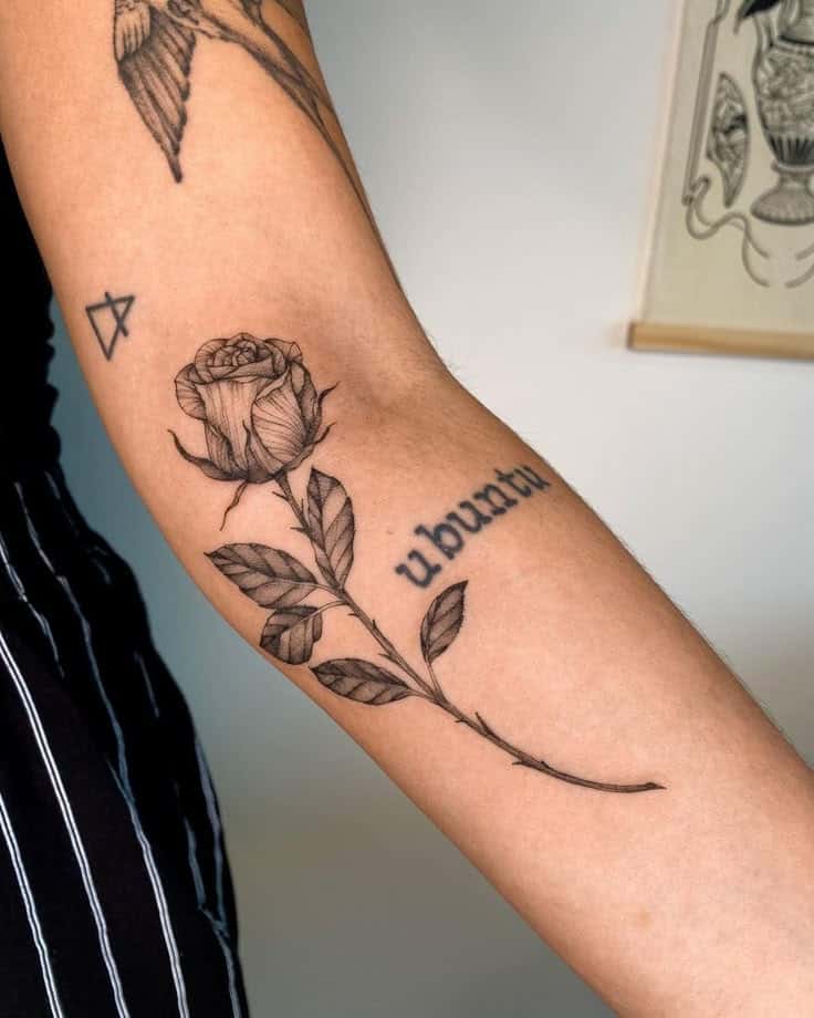 Close-up of an arm tattoo featuring a detailed rose with leaves and the word ubuntu, symbolizing connection and community.