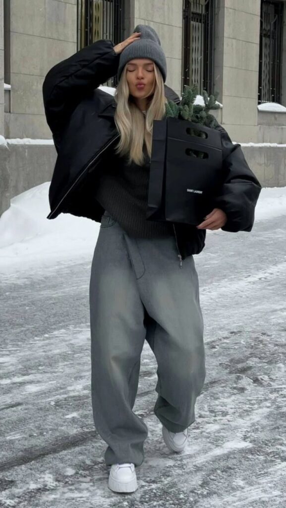 Trendy winter outfit with oversized jacket, beanie, and baggy jeans on snowy street. Fashionable cold-weather style.
