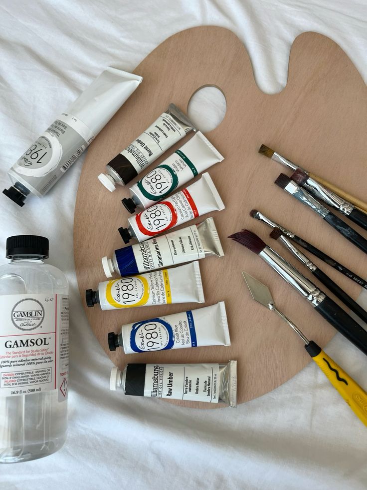 Art supplies on a wooden palette: tubes of paint, brushes, and a bottle of solvent on a white background. Perfect for painting projects.