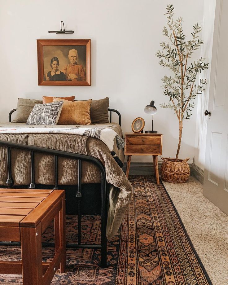_ 19 Cozy rustic bedroom with vintage decor, framed art, wooden nightstand, patterned rug, and potted tree. | Sky Rye Design Cozy rustic bedroom with vintage decor, framed art, wooden nightstand, patterned rug, and potted tree.