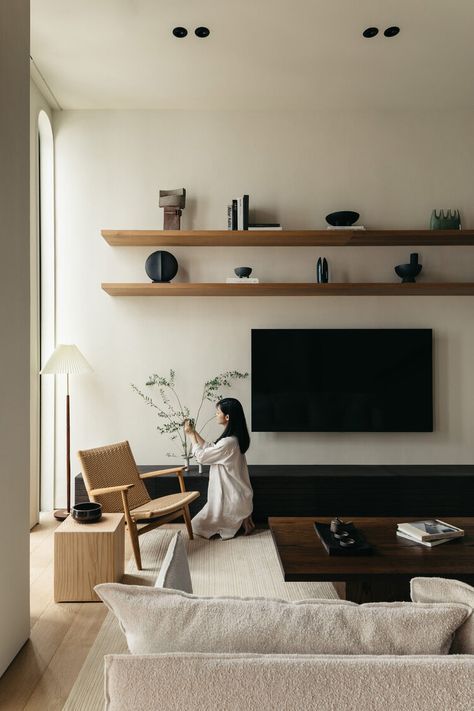 _ 19 Modern living room with minimalist decor, woman arranging plants near a chair, wall shelves and TV. Cozy and stylish interior. | Sky Rye Design Modern living room with minimalist decor, woman arranging plants near a chair, wall shelves and TV. Cozy and stylish interior.