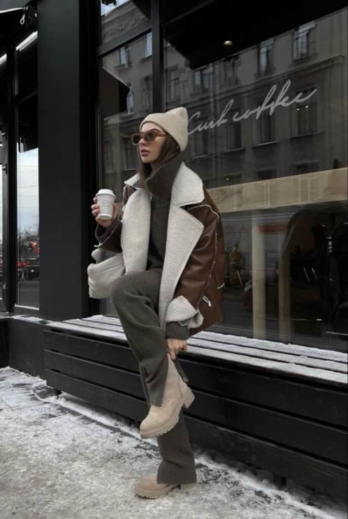 Stylish woman in winter outfit with coat and beanie holds coffee outside chic cafe.