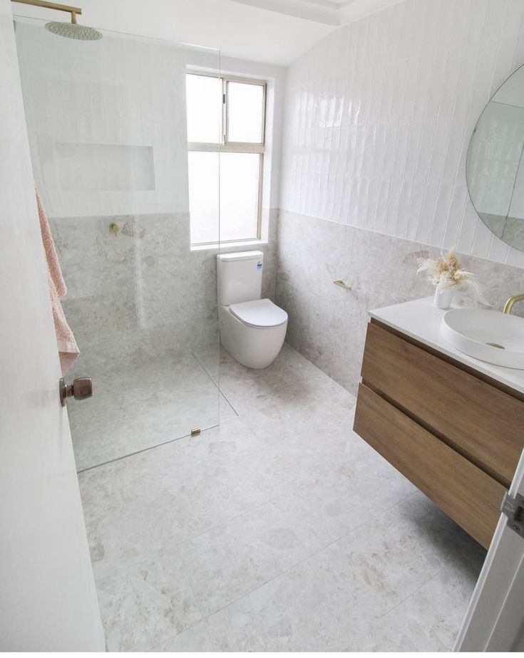 Modern minimalist bathroom design with glass shower, wooden vanity, and white tiles.
