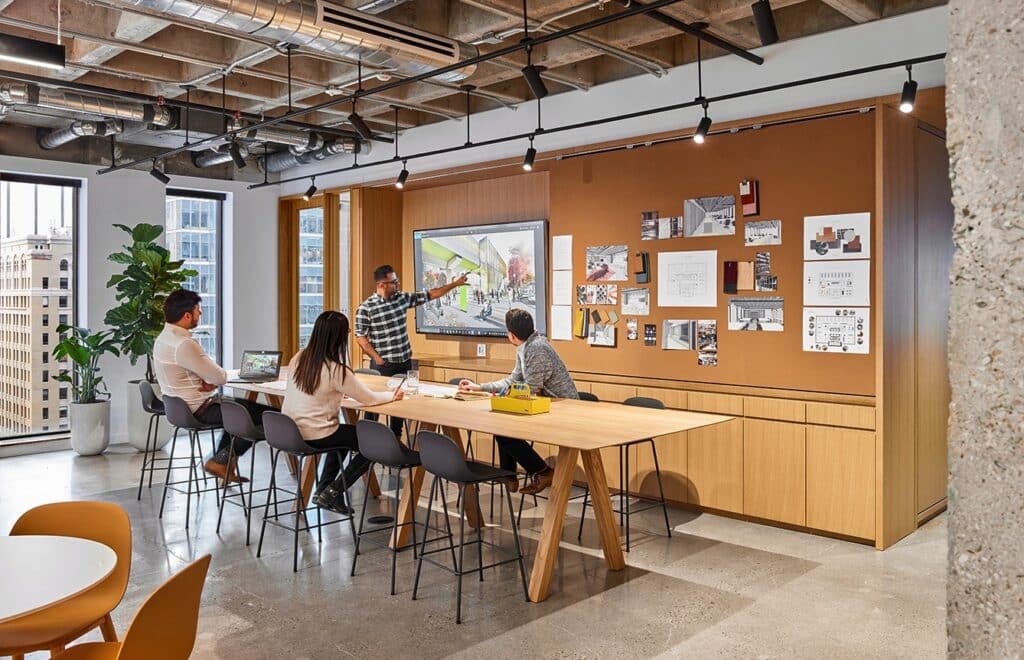 Office meeting with four colleagues collaborating around a table, discussing a digital presentation in a modern workspace environment.