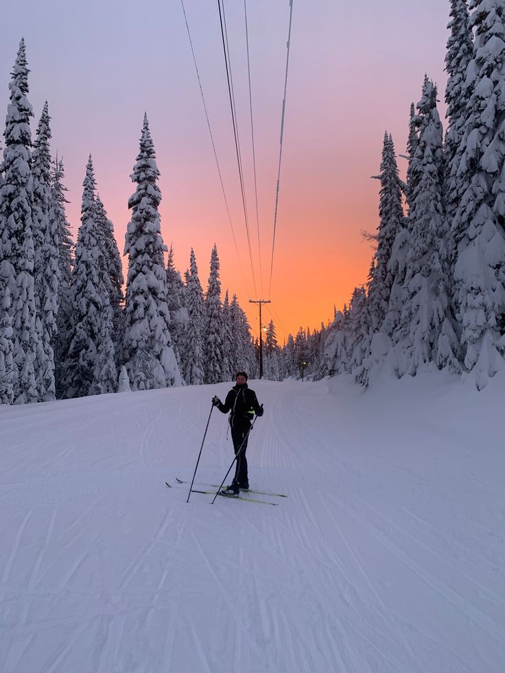 Cross-country skier on snowy trail during vibrant sunset, surrounded by snow-covered trees and power lines, in a winter wonderland scene.