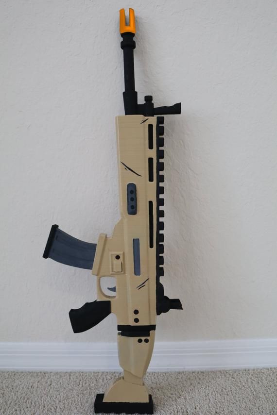 Toy rifle with beige and black design featuring orange tip, leaning against a wall on a carpeted floor.