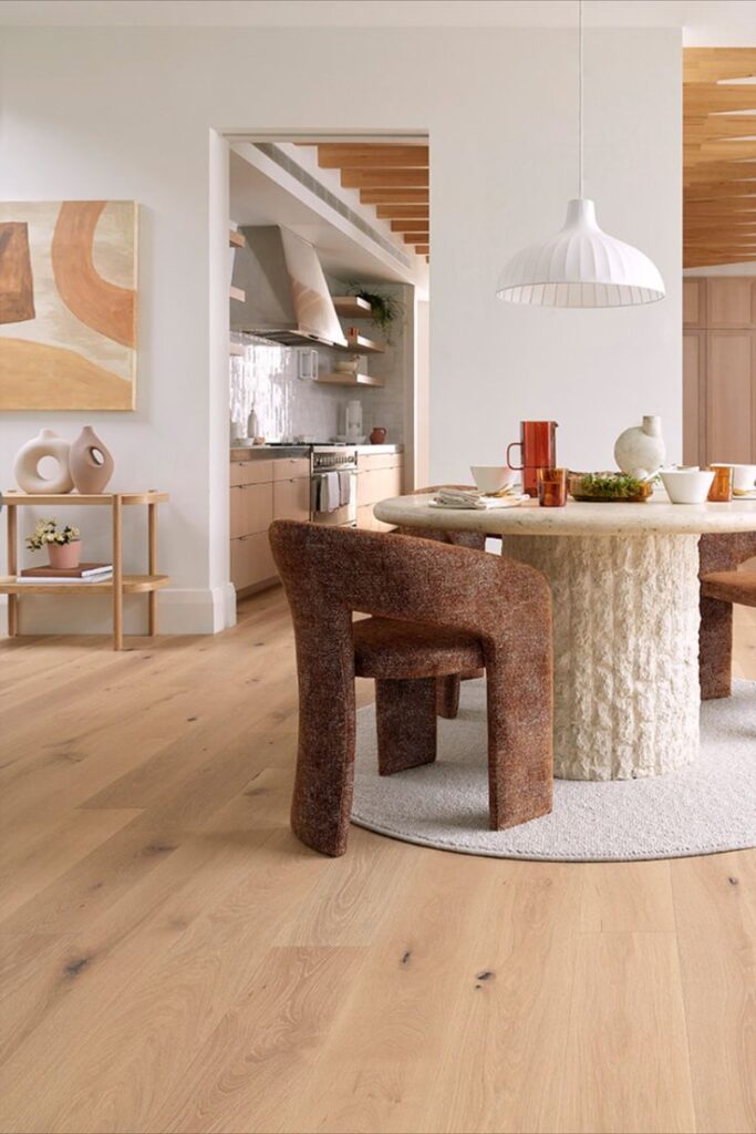 Modern dining room with round table, textured chairs, pendant light, and contemporary decor. Warm, minimalist design.