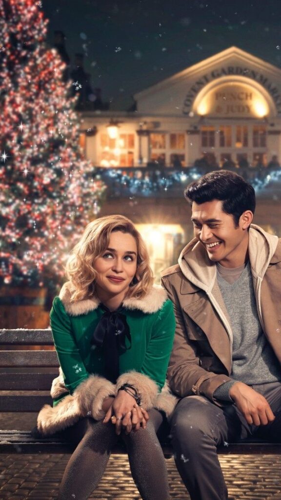 _ 2 Couple sitting on a bench with a Christmas tree and festive lights in the background, smiling warmly at each other. | Sky Rye Design Couple sitting on a bench with a Christmas tree and festive lights in the background, smiling warmly at each other.
