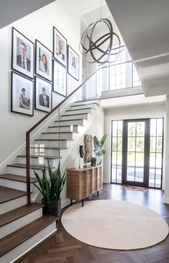 Modern entryway with a staircase, framed photos, and stylish decor. Features large windows and contemporary lighting fixture.