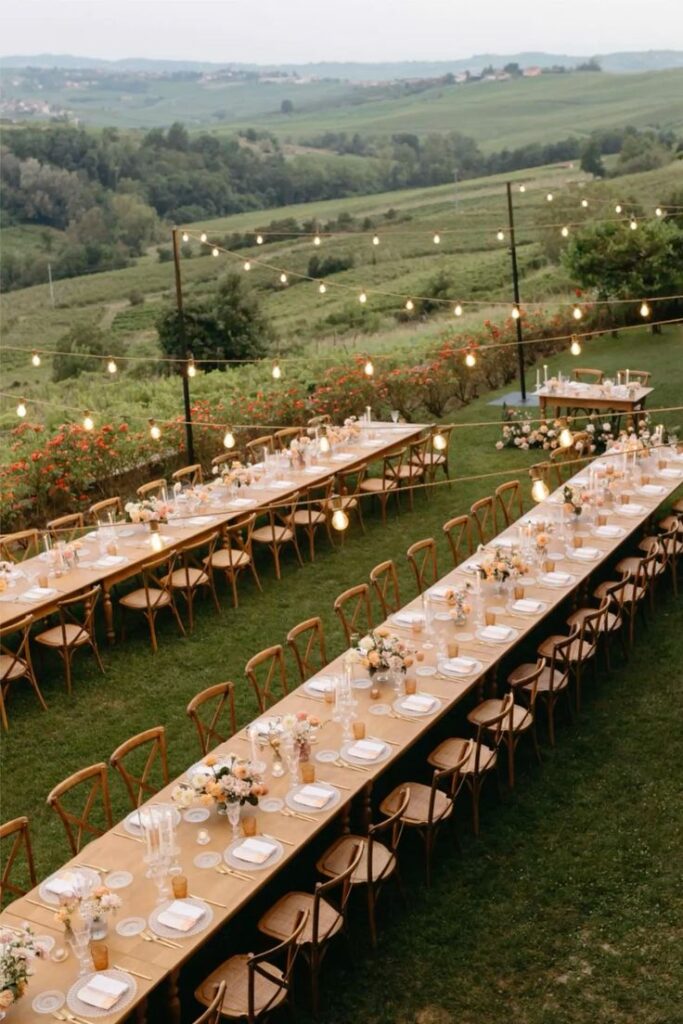 _ 2 Elegant outdoor wedding reception setup with long tables, floral centerpieces, and string lights overlooking a scenic countryside landscape. | Sky Rye Design Elegant outdoor wedding reception setup with long tables, floral centerpieces, and string lights overlooking a scenic countryside landscape.