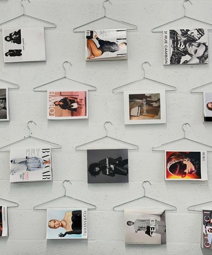 Fashion magazine covers hung creatively on hangers against a white wall, showcasing various brands and styles in a modern display.