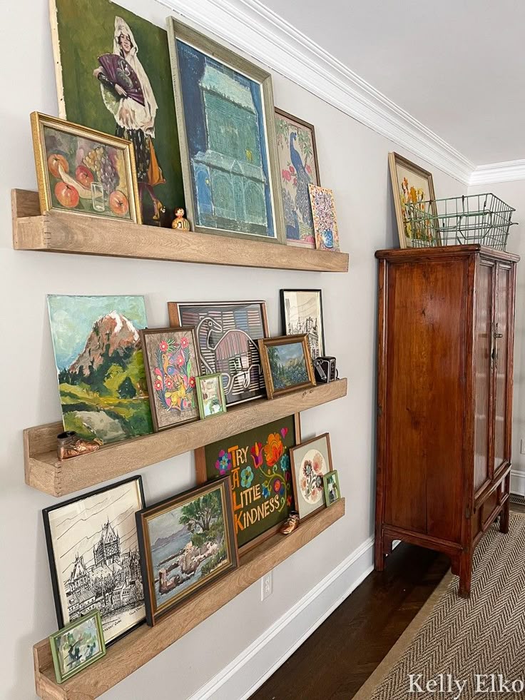 _ 20 Wooden shelves displaying assorted colorful artworks and decor against a white wall, next to a vintage cabinet. | Sky Rye Design Wooden shelves displaying assorted colorful artworks and decor against a white wall, next to a vintage cabinet.
