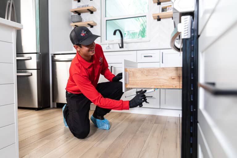 Professional pest control technician inspecting a kitchen drawer, wearing gloves and a uniform, ensuring a pest-free environment.