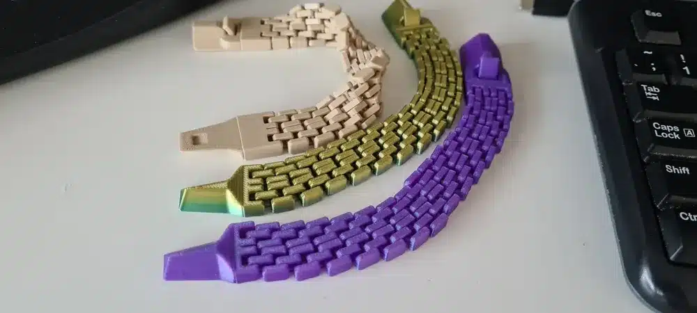 Three colorful, woven 3D-printed objects in beige, green, and purple, displayed on a desk next to a keyboard.