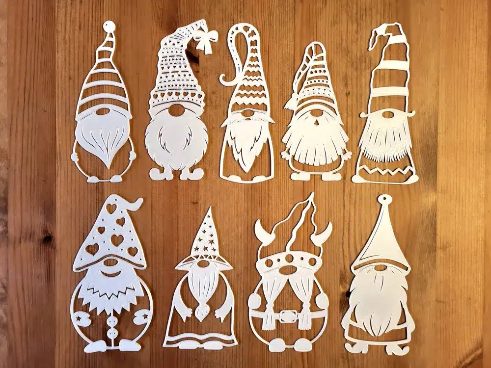 Paper cutouts of whimsical gnome designs on wooden table, featuring various hats and beards, perfect for craft and holiday decor.