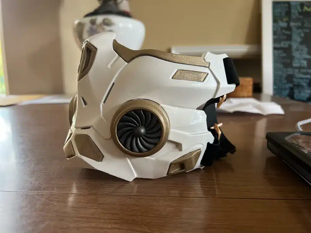 2024-03-10_ed892bc48e83e Futuristic white and gold mask with turbine design on wooden table. | Sky Rye Design Futuristic white and gold mask with turbine design on wooden table.