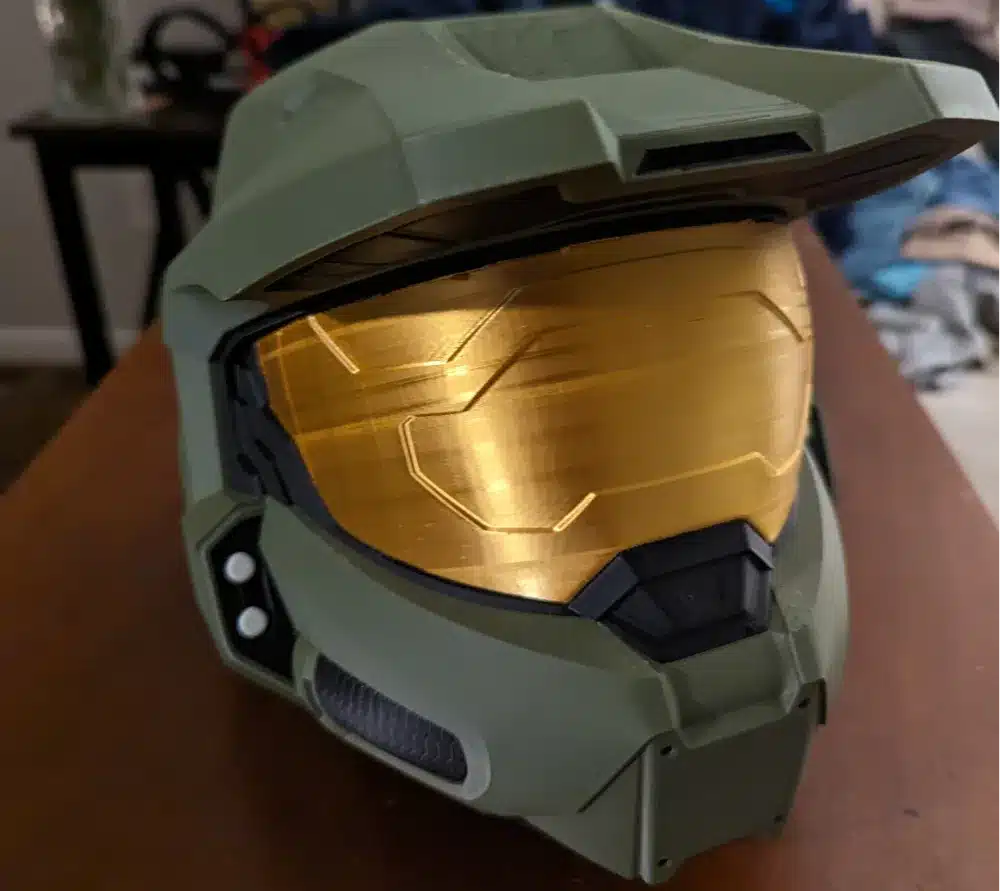 Green sci-fi helmet with gold visor on wooden table, showcasing sleek design and futuristic aesthetics.