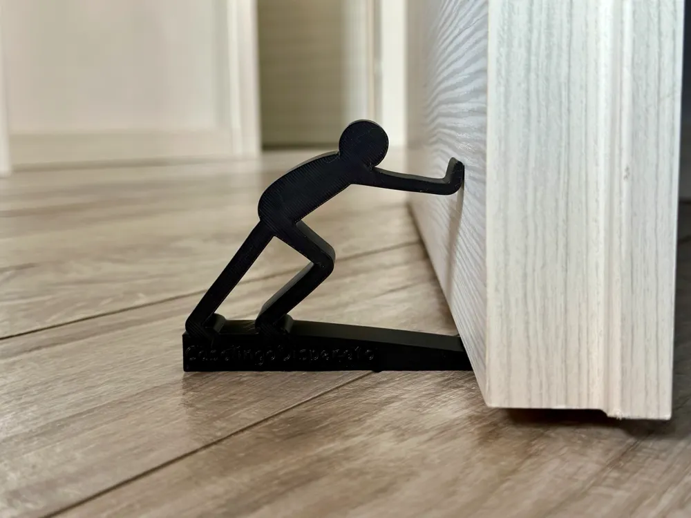 Black doorstop in the shape of a person pushing, holding open a white door on wooden floor. Unique and functional home accessory.