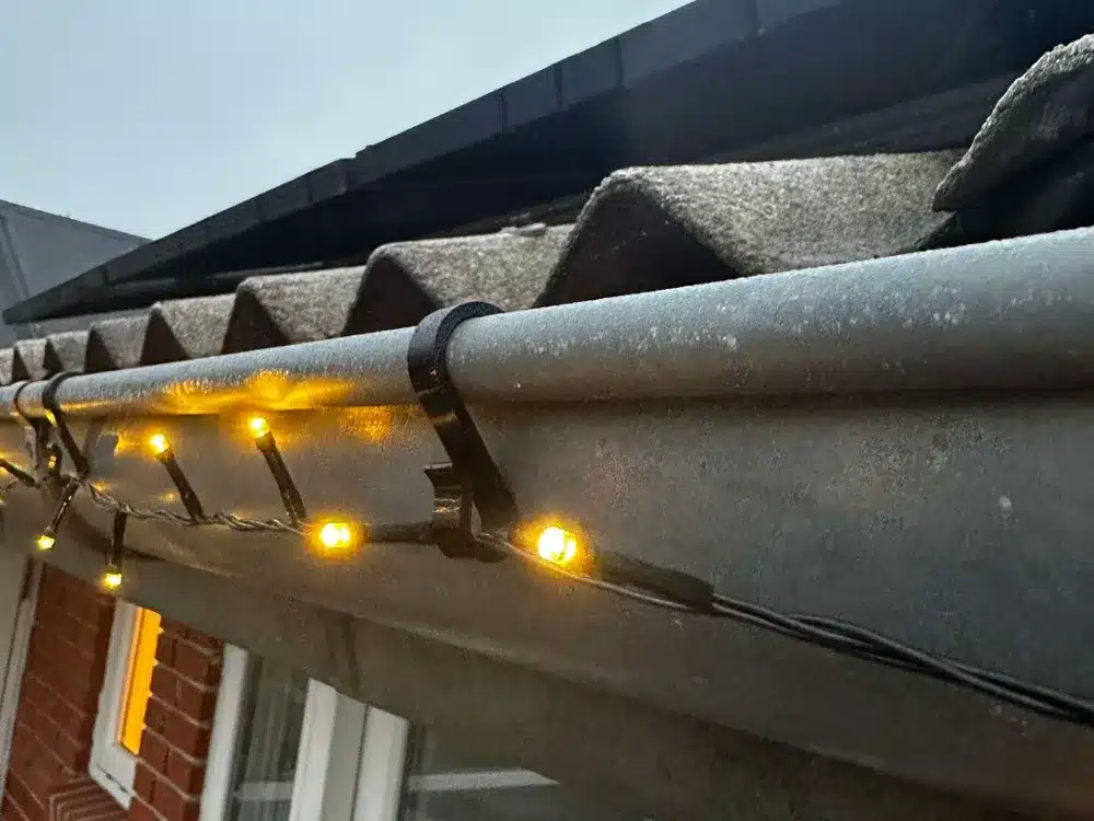Yellow string lights hanging on a roof gutter, creating a festive atmosphere during dusk.