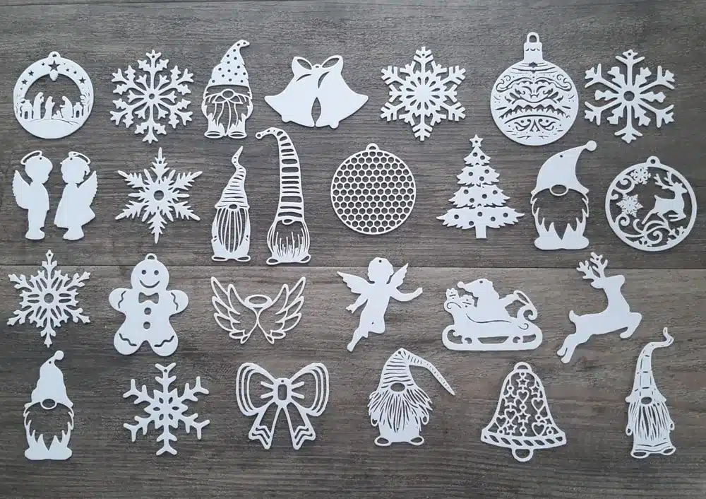 White Christmas-themed paper cutouts on a wooden surface, featuring snowflakes, angels, gnomes, and holiday symbols.