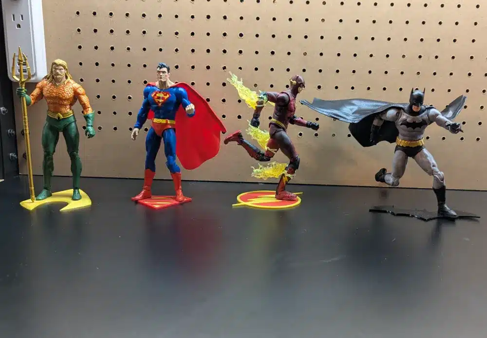 Four superhero action figures posed dynamically in front of a pegboard on a black tabletop.