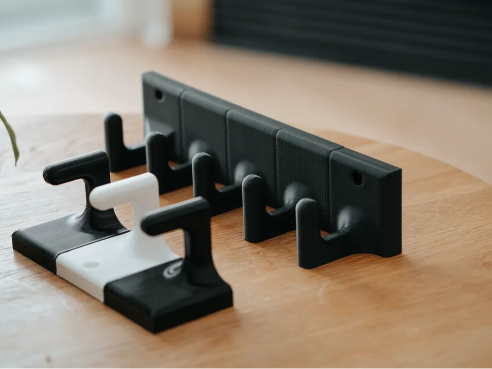 Black and white 3D-printed guitar wall hangers on a wooden table, designed for space-saving and secure instrument storage.