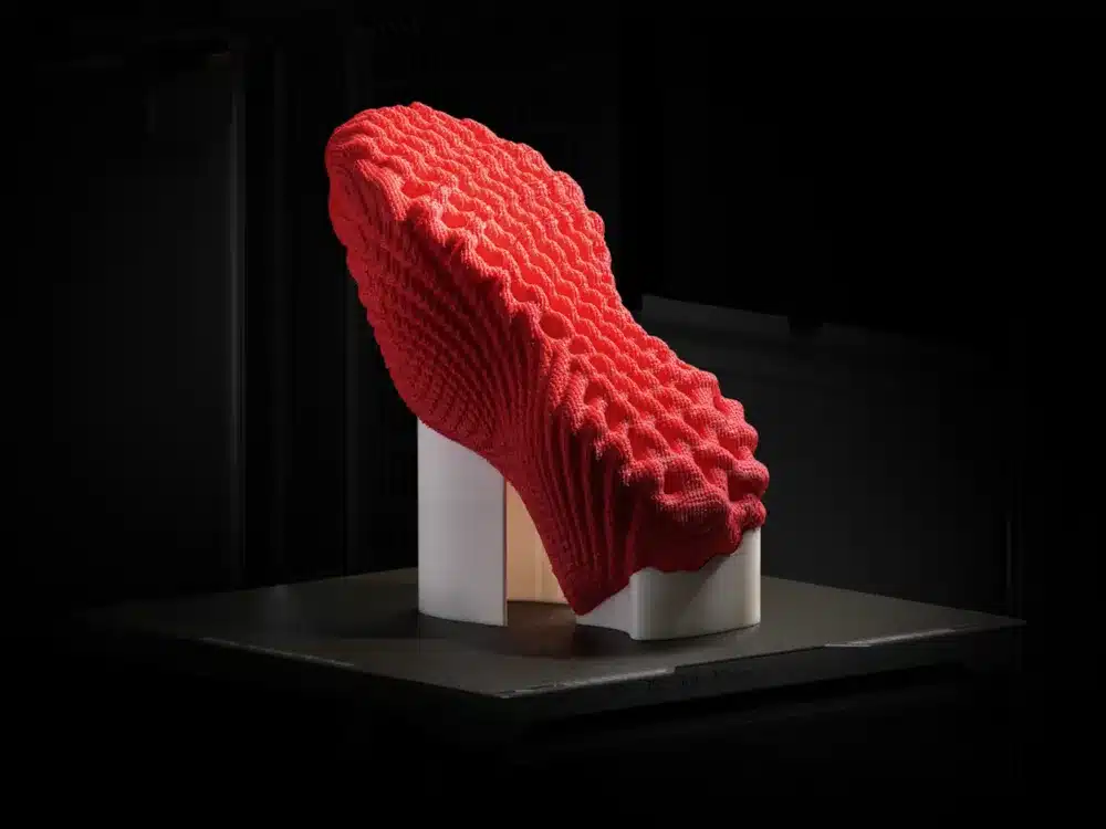 Innovative red 3D-printed sneaker design on a black background, showcasing textured knit structure.