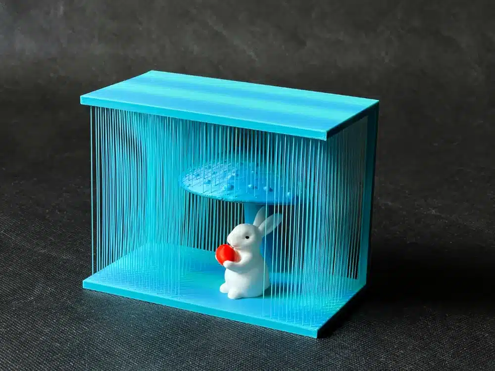 White bunny under a blue string art installation, holding a red object.