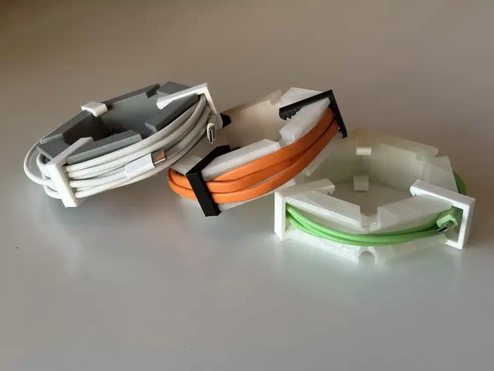 Three coiled cables in white, orange, and green are neatly organized in 3D-printed holders on a white surface.