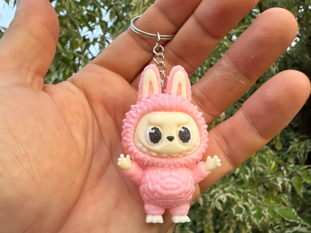 Cute pink bunny keychain toy held in hand outdoors with lush green background. Perfect for gifts or adorable accessory collectors.