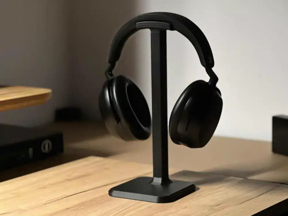 Black over-ear headphones on a sleek stand, placed on a wooden desk, creating a modern and minimalistic workspace aesthetic.