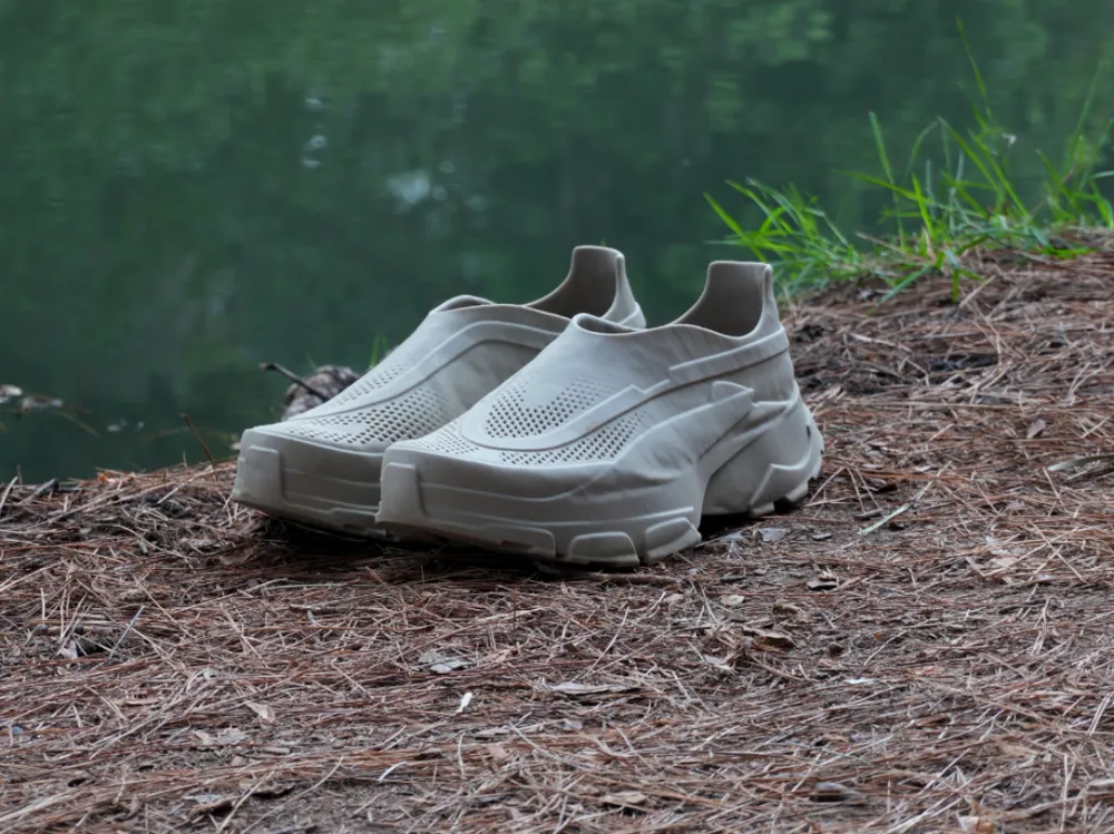 Minimalist beige sneakers on a forest floor, near a serene lake. Perfect for outdoor adventures and casual fashion.