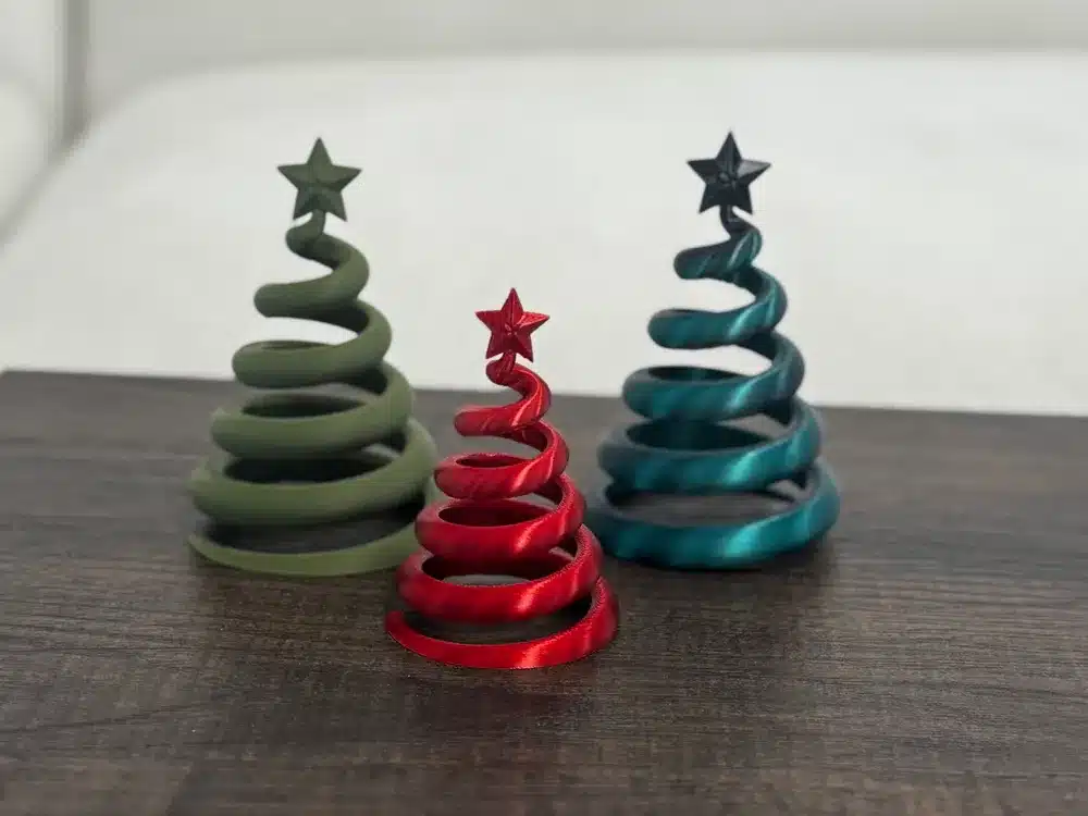 Three spiral Christmas tree ornaments in green, red, and blue with stars on top, on a wooden surface. Festive home decor.